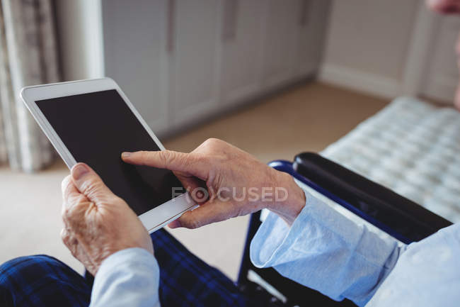 Close-up de homem idoso sentado em cadeira de rodas e usando comprimido digital em casa — Fotografia de Stock