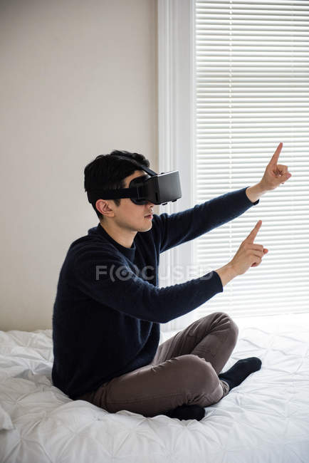 Hombre usando auriculares de realidad virtual en el dormitorio en casa - foto de stock