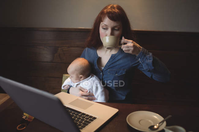 Mãe tomando café enquanto segura o bebê no café — Fotografia de Stock