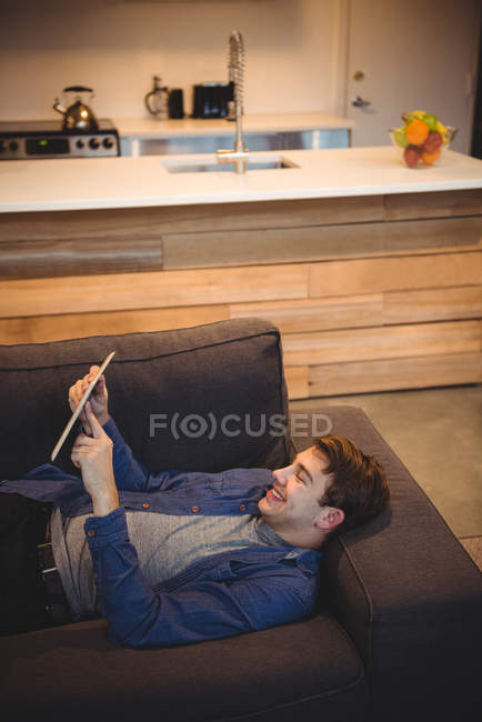 Улыбающийся мужчина лежит на диване, используя цифровой планшет в гостиной дома — стоковое фото