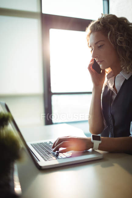 Виконавчий директор бізнесу розмовляє на мобільному телефоні під час роботи на ноутбуці в офісі — стокове фото