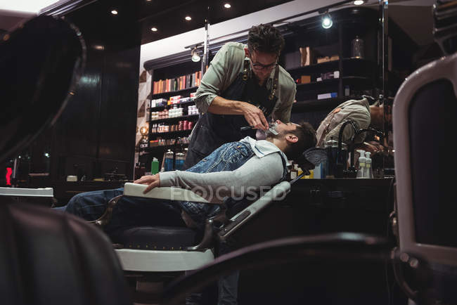 Hombre conseguir barba afeitado por peluquero con maquinilla de afeitar en peluquería - foto de stock