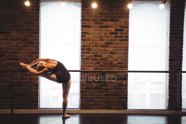 Bailarina estirándose en barra en estudio de ballet - foto de stock