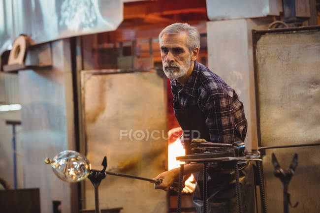Стеклодув, формирующий расплавленное стекло на стекольном заводе — стоковое фото