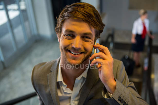 Businessman on escalator talking on mobile phone in airport — Stock Photo