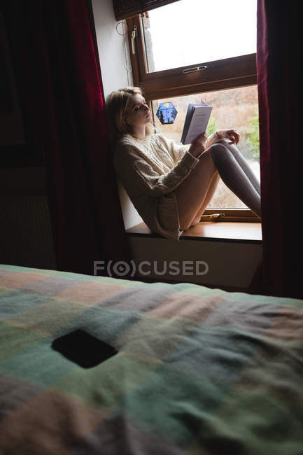 Mulher sentada na janela e lendo um livro em casa — Fotografia de Stock