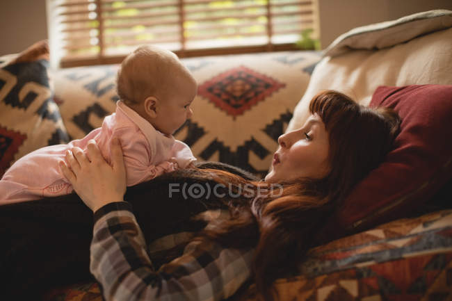 Madre jugando con la hija bebé en el sofá en la sala de estar - foto de stock