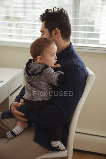 Padre che tiene in braccio il bambino mentre è seduto alla scrivania — Foto stock