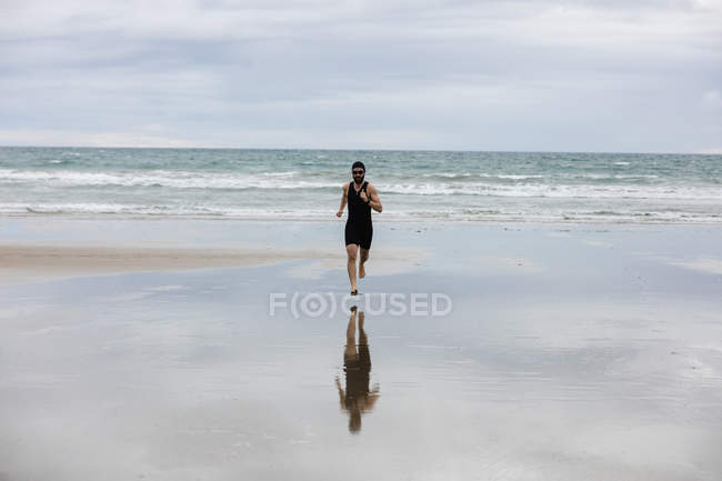 Man in swimming costume and swimming cap running on beach — Stock Photo