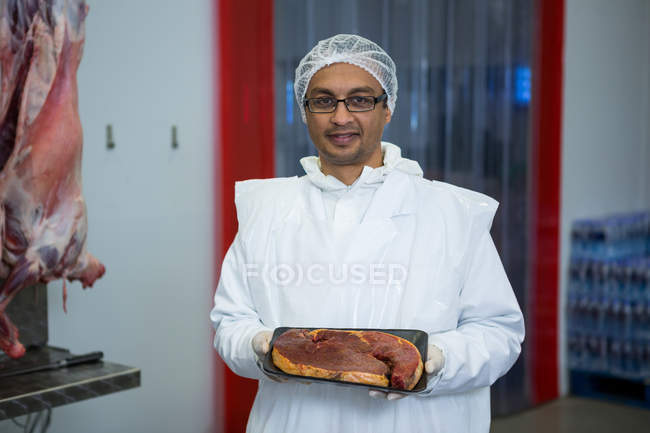 Ritratto di macellaio che tiene il vassoio di carne in fabbrica di carne — Foto stock