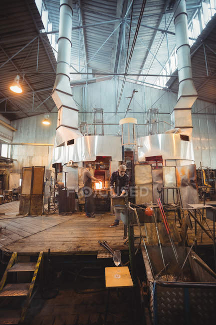 Команда стеклодувов, формирующих стекло на трубе на стеклодувном заводе — стоковое фото
