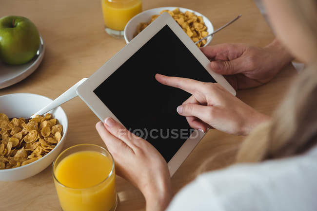 Couple using digital tablet while having breakfast at home — Stock Photo
