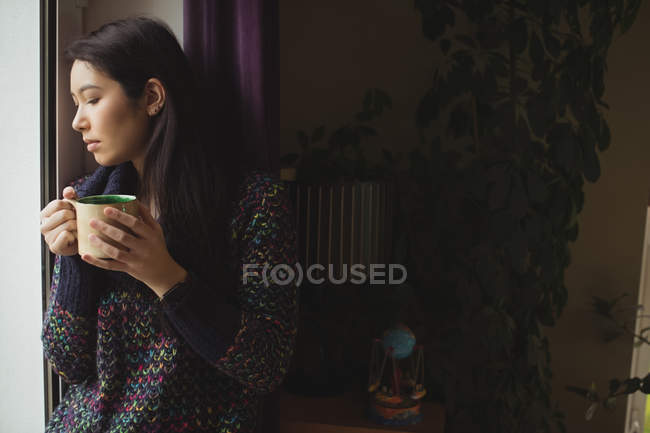 Женщина за чашкой кофе у окна дома — стоковое фото