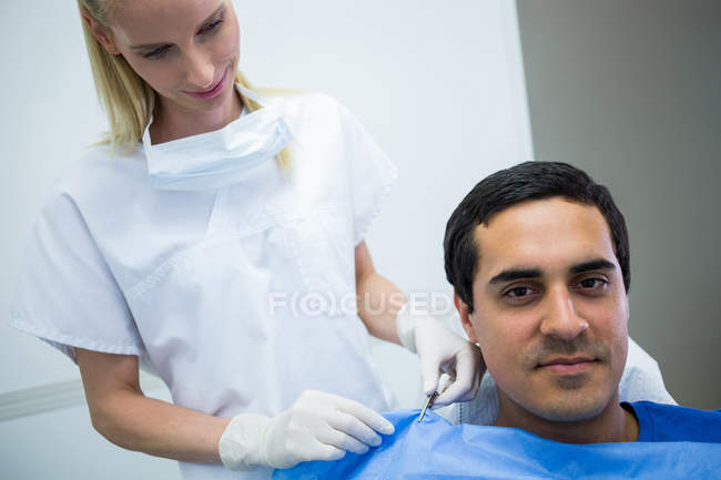 Dentista que ayuda al paciente a usar delantal dental en la clínica - foto de stock