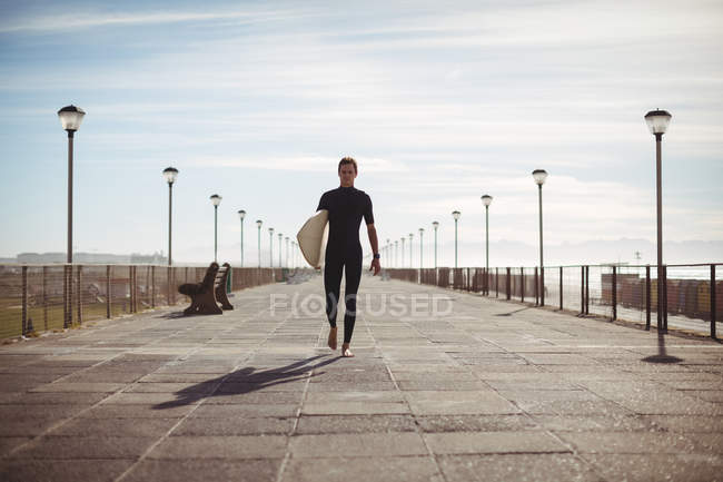 Surfista caminando con tabla de surf en el muelle en la playa - foto de stock