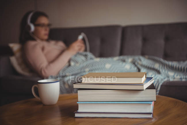 Stapel Bücher auf dem Tisch, während die Frau zu Hause im Hintergrund Musik hört — Stockfoto