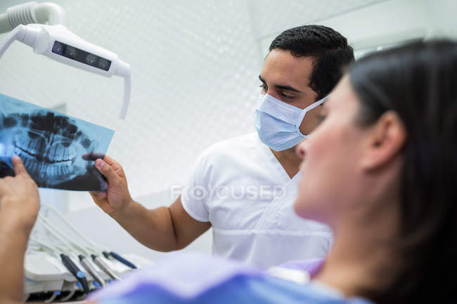 Junger männlicher Zahnarzt untersucht Röntgenbild mit Patientin in der Klinik — Stockfoto