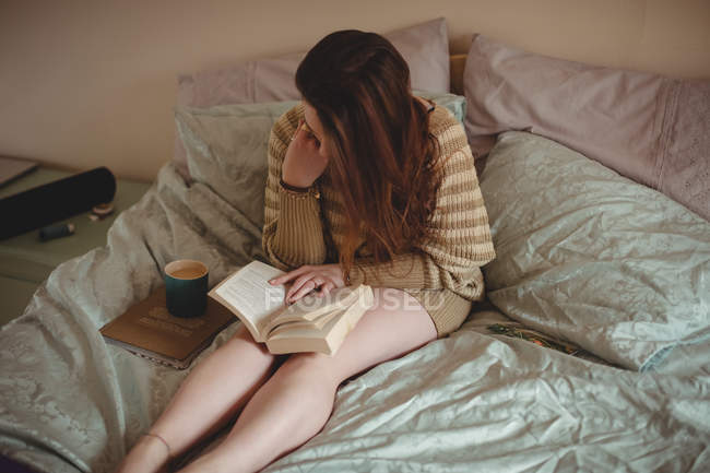 Женщина сидит на кровати и читает книгу дома — стоковое фото