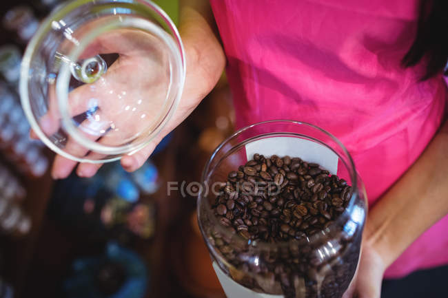 Close-up of female shopkeeper holding jar of coffee beans at counter in shop — Stock Photo