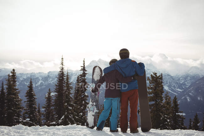 Vue arrière du couple tenant le snowboard en montagne pendant l'hiver contre le ciel — Photo de stock