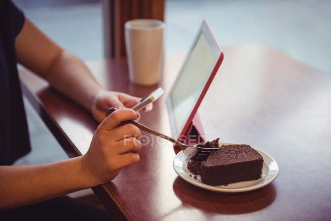 Крупним планом жінка має десерт і використовує мобільний телефон в ресторані — стокове фото