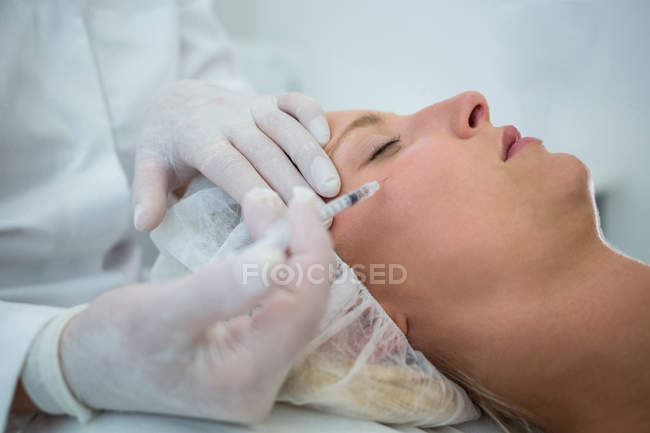 Primer plano de la paciente adulta media que recibe la inyección de botox en la cara - foto de stock