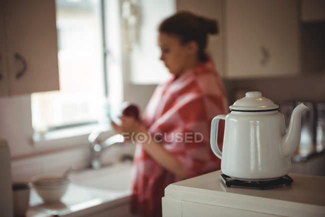 Chaleira no fogão e mulher de pé no fundo na cozinha em casa — Fotografia de Stock