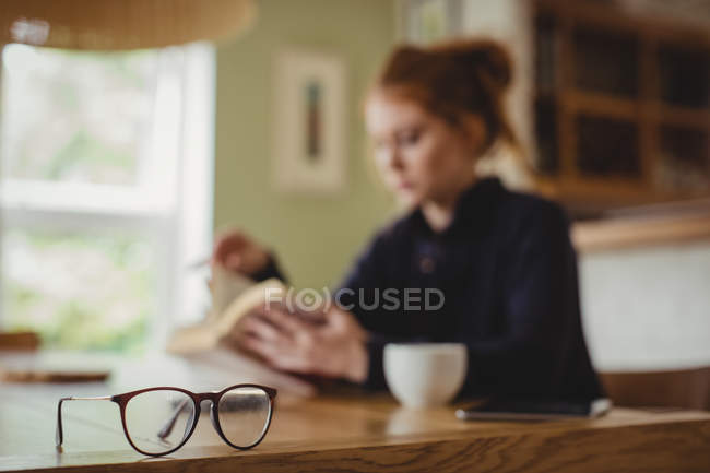 Woman sitting by dining table and reading a book at home — Stock Photo