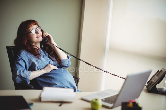 Pregnant businesswoman touching belly while talking on telephone in office — Stock Photo