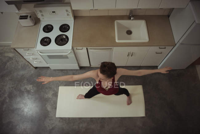 Высокоугольный вид женщины, выполняющей растягивающую позу йоги на кухне дома — стоковое фото