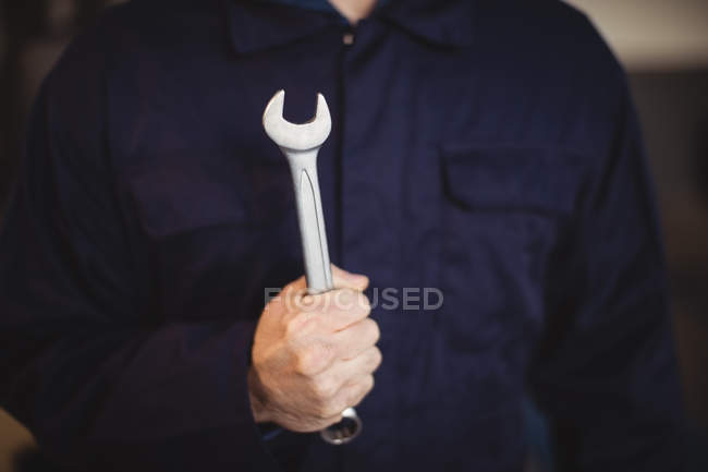 Mid-section of mechanic holding a wrench tool in repair garage — Stock Photo