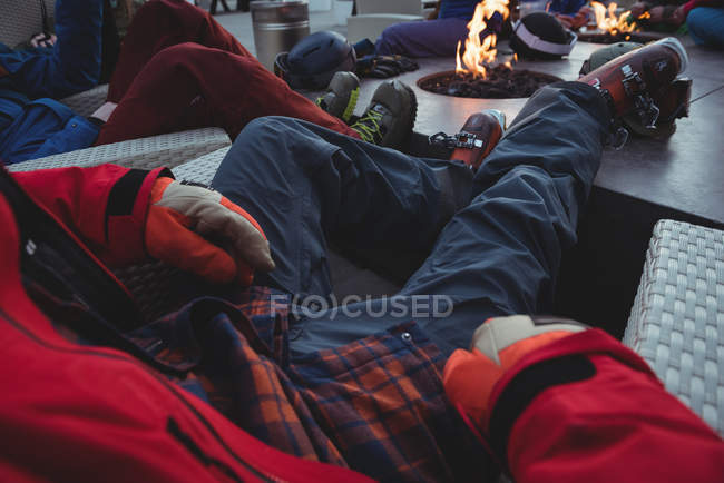 Low section of skiers relaxing in ski resort by fire — Stock Photo