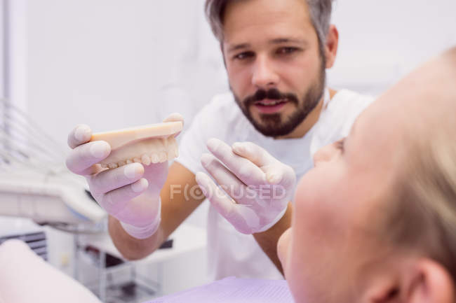 Dentista che mostra il modello di protesi al paziente in clinica — Foto stock