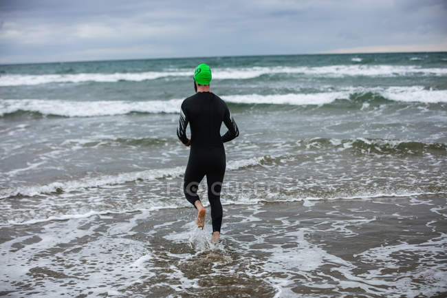 Visão traseira do atleta em terno molhado correndo em direção ao mar — Fotografia de Stock