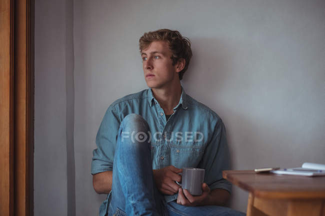 Un hombre reflexivo sosteniendo una taza de café en casa - foto de stock