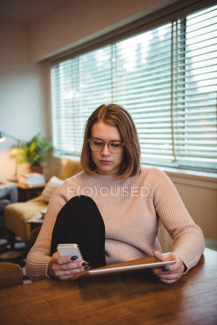 Woman sitting on chair using mobile phone and digital tablet in living room — Stock Photo