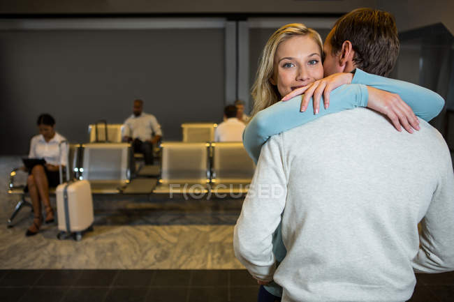 Pareja feliz abrazándose en la sala de espera en la terminal del aeropuerto - foto de stock