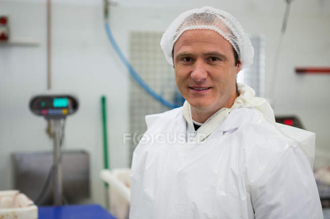 Retrato del carnicero sonriente de pie en la fábrica de carne - foto de stock