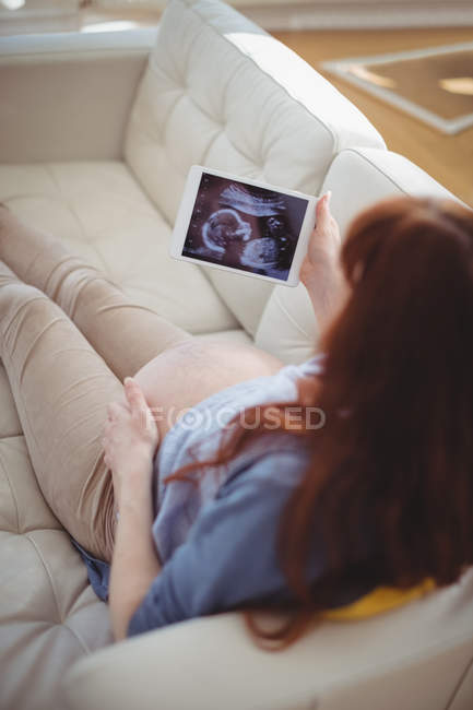 Беременная женщина смотрит на сонографию на цифровом столе в гостиной — стоковое фото