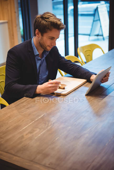 Empresário usando tablet digital enquanto faz lanche no café — Fotografia de Stock
