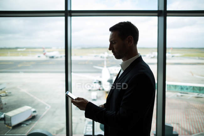 Uomo d'affari con bagagli utilizzando il telefono cellulare in aeroporto — Foto stock