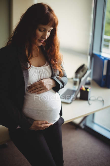Schwangere Geschäftsfrau berührt Bauch im Büro — Stockfoto