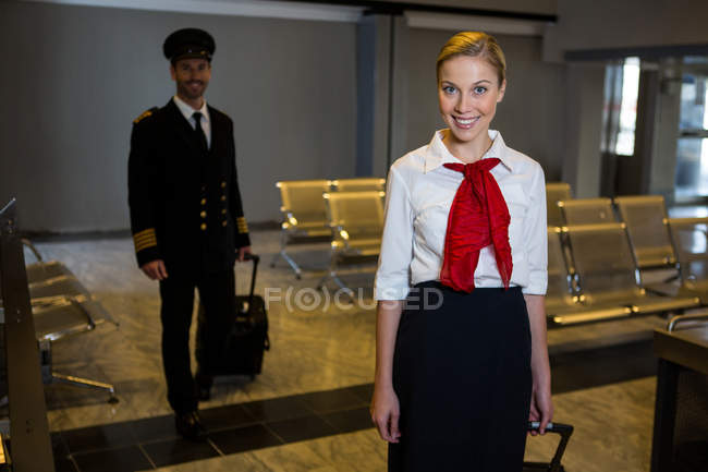 Portrait of pilot and air hostess walking with their trolley bags in the airport terminal — Stock Photo
