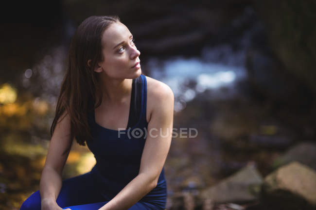 Thoughtful woman sitting on rock in forest — Stock Photo