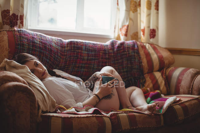 Frau hält Kaffeetasse und liegt zu Hause auf Sofa — Stockfoto