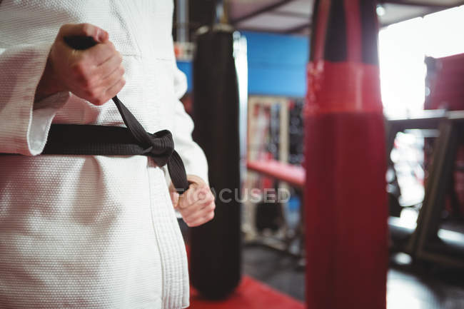 Средняя секция игрока в карате, завязывающего пояс в фитнес-студии — стоковое фото