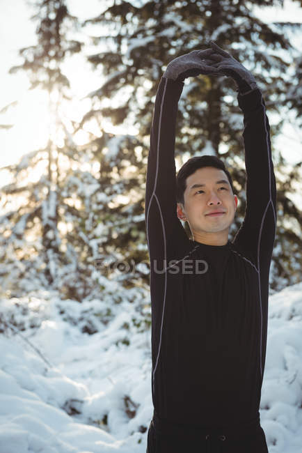 Homem sorridente esticando os braços na floresta durante o inverno — Fotografia de Stock