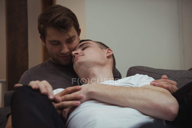 Романтическая гей-пара, обнимающаяся на диване в гостиной дома — стоковое фото