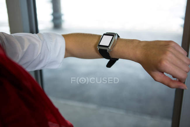 Sección media de la azafata del aire que comprueba el tiempo en smartwatch en la terminal del aeropuerto - foto de stock