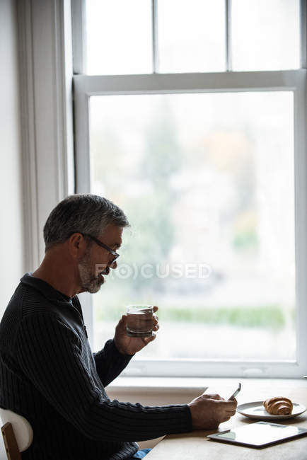 Людина використовує мобільний телефон, маючи склянку води вдома — стокове фото